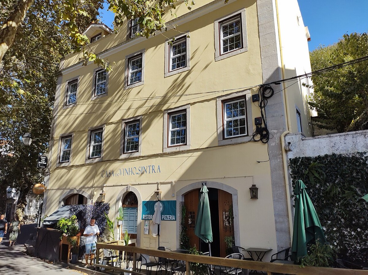 Fachada amarela de uma guest house no centro de Sintra, com esplanada e chapéus de sol verdes