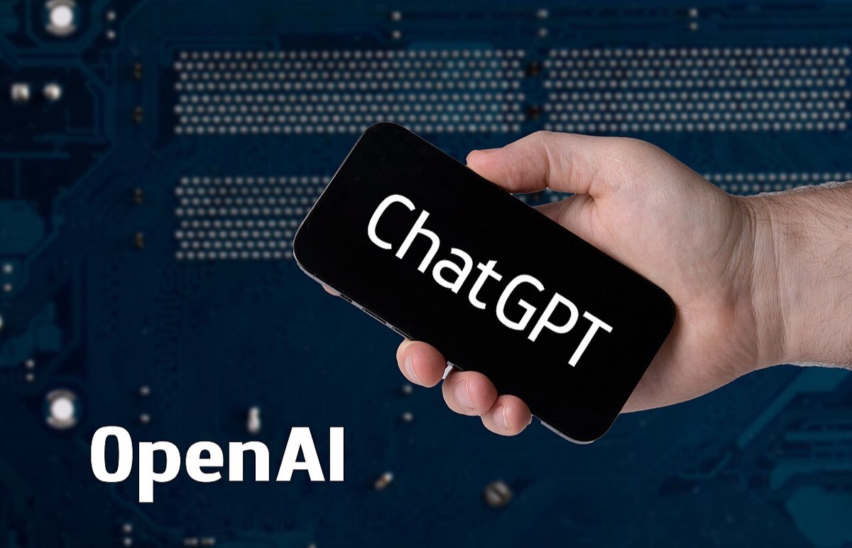 Mão a segurar um telemóvel com o ChatGPT aberto, com o logótipo da OpenAI ao fundo