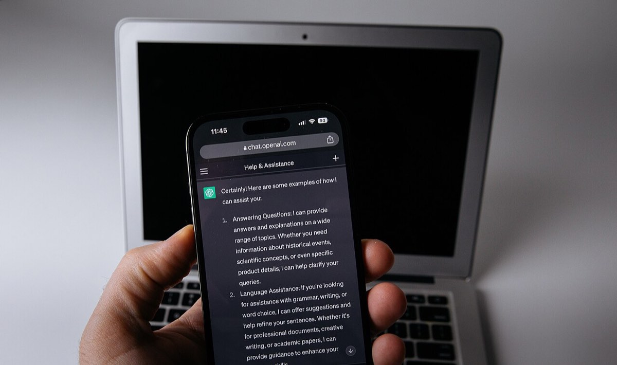 Telemóvel com a aplicação do ChatGPT aberta ao lado de um portátil