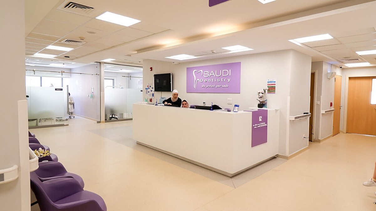 Receção ampla e luminosa de uma clínica dentária, com balcão branco e cadeiras de espera roxas