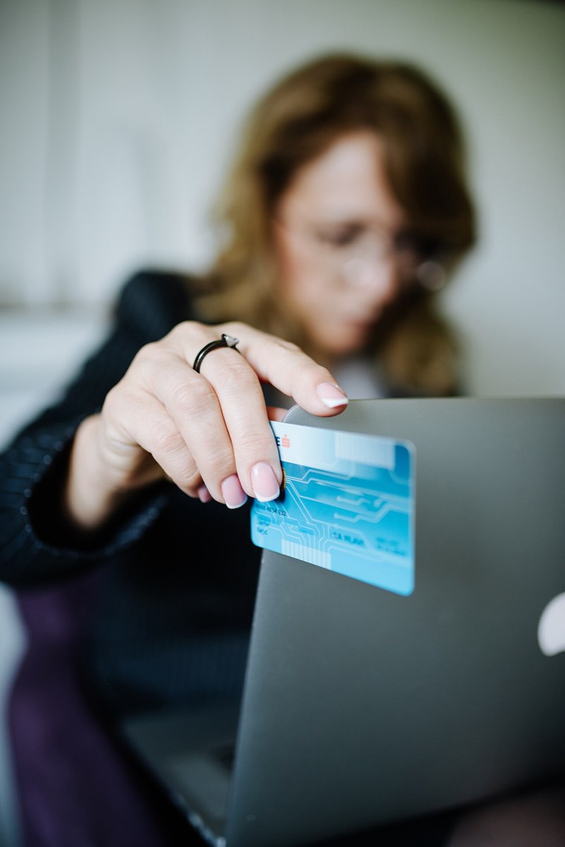 Pessoa com um cartão de pagamento na mão a fazer uma compra num portátil