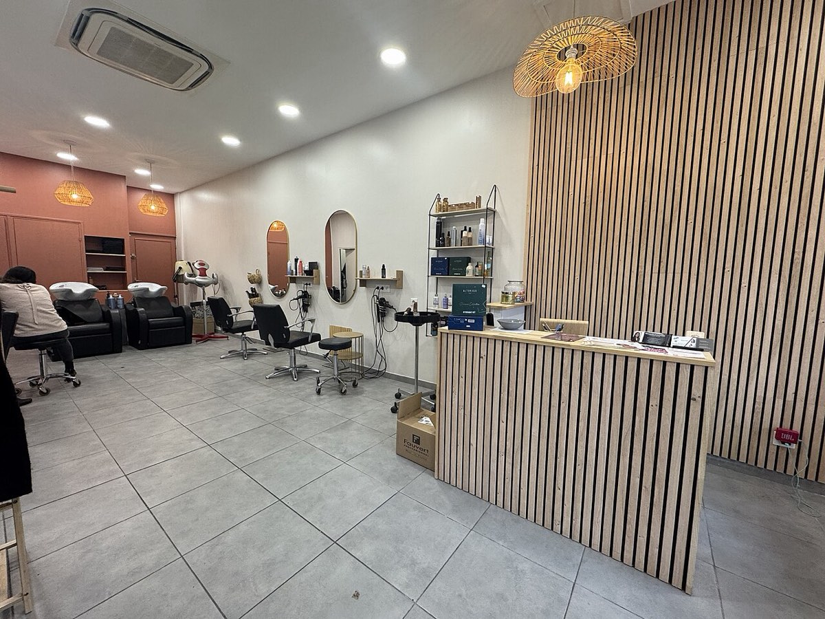 Interior de um salão de cabeleireiro moderno com cadeiras pretas, lavatórios, espelhos ovais e balcão de receção em madeira